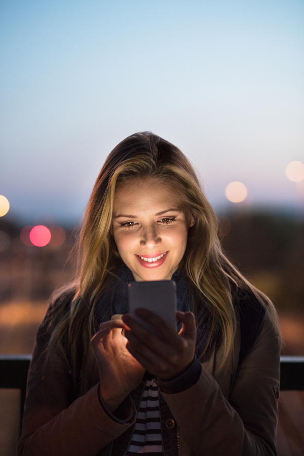 Beautiful woman in the city at night holding smartphone, texting.