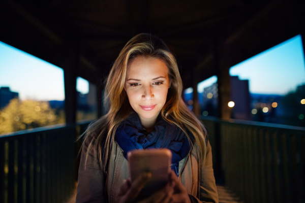 Beautiful woman in the city at night holding smartphone, texting.