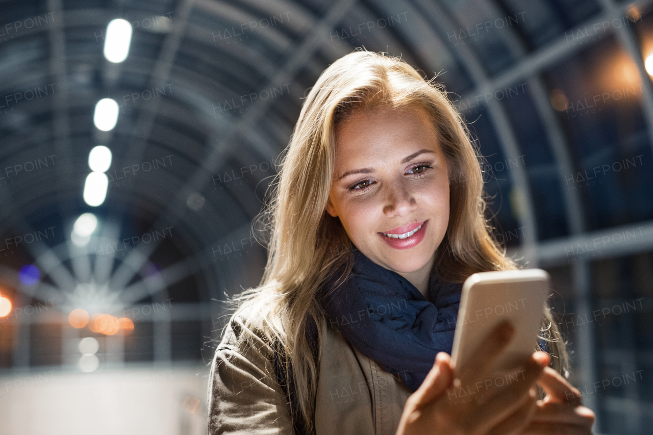 Beautiful woman in the city at night holding smartphone, texting.