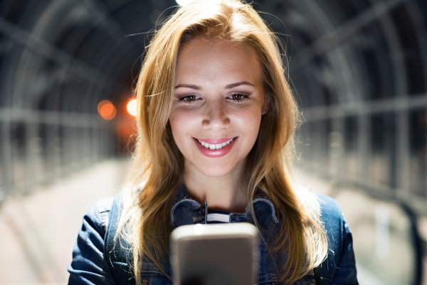 Beautiful woman in the city at night holding smartphone, texting.