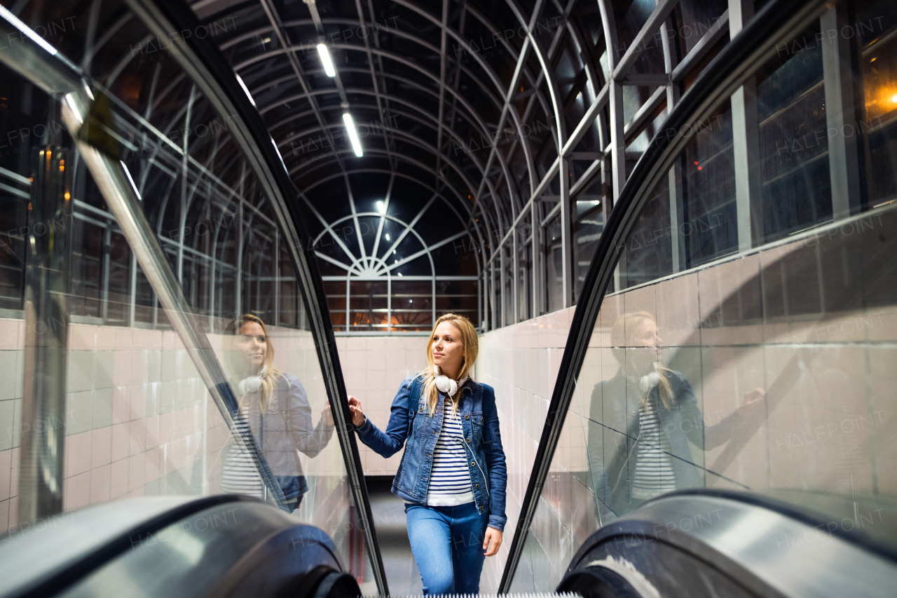 Beautiful woman in the city at night on escalator in bus station earphones on her neck.