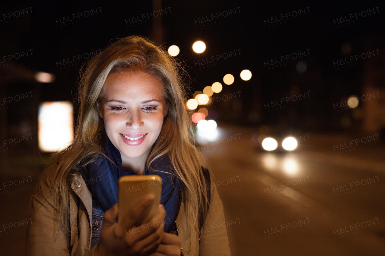 Beautiful woman in the city at night holding smartphone, texting.