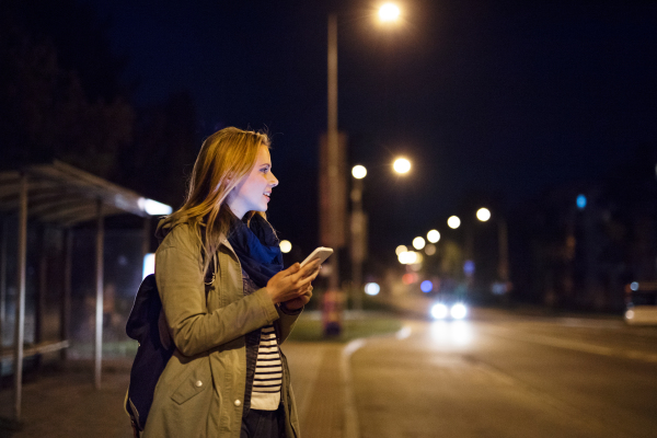 Beautiful woman in the city at night holding smartphone, texting.