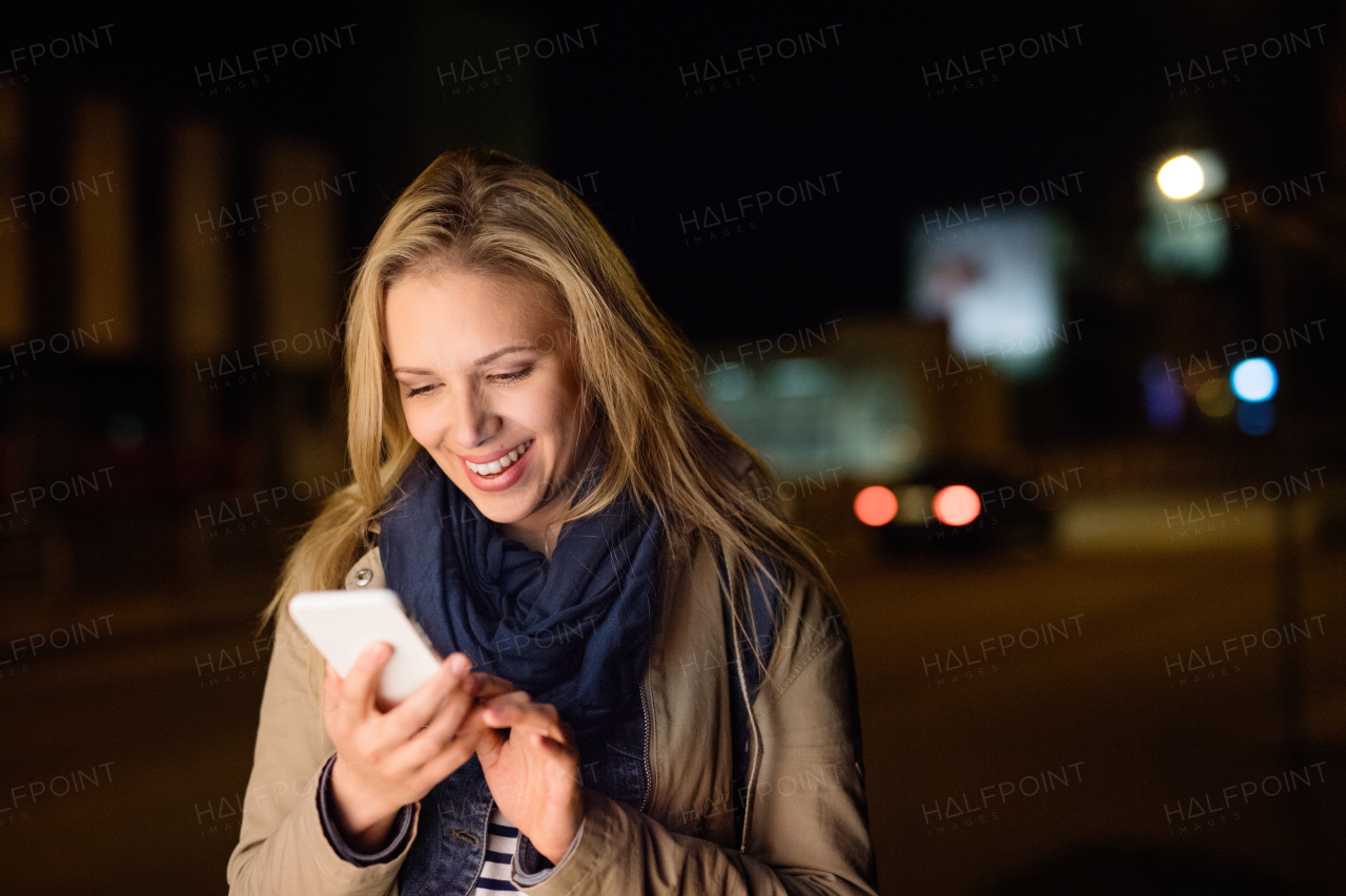 Beautiful woman in the city at night holding smartphone, texting.