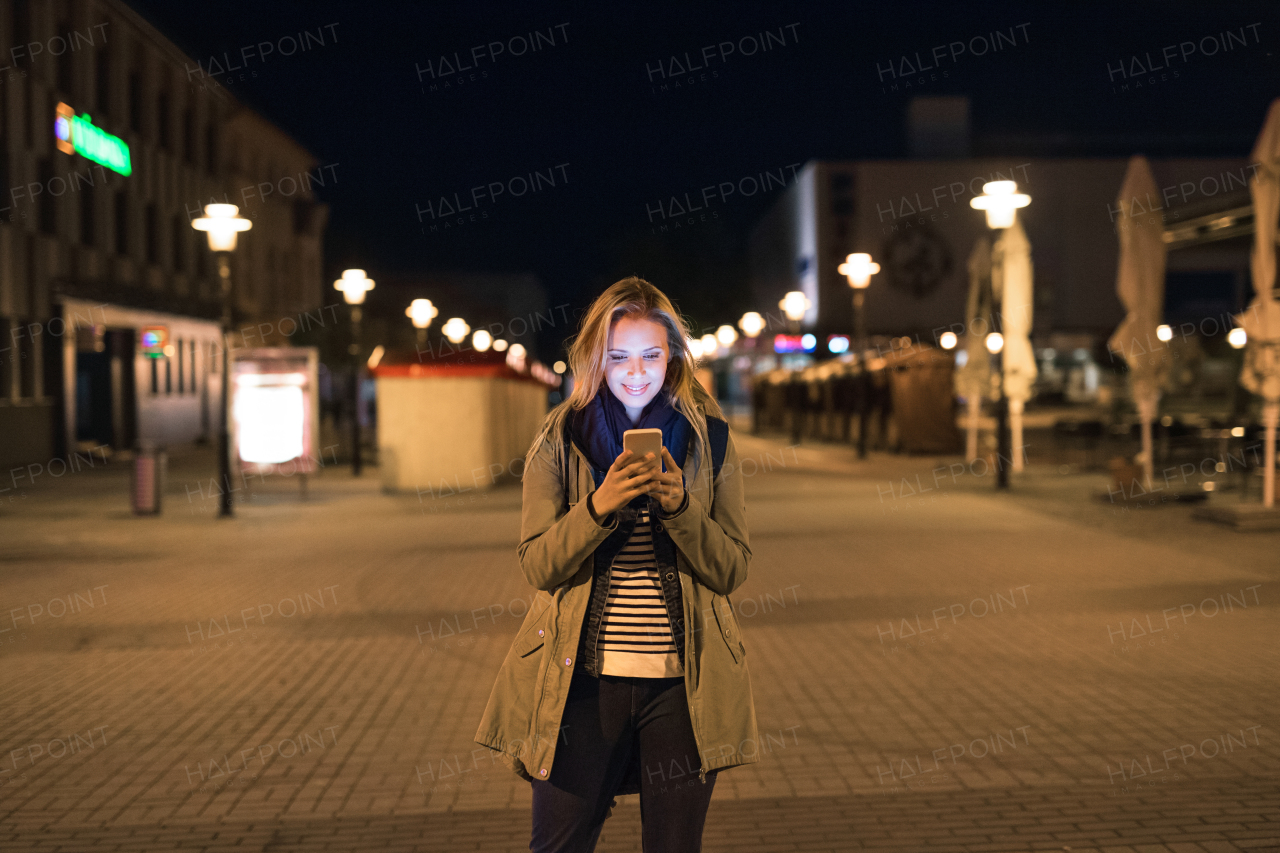 Beautiful woman in the city at night holding smartphone, texting.