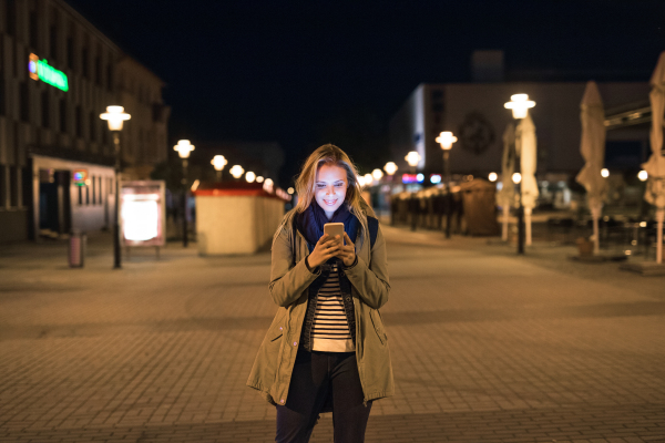 Beautiful woman in the city at night holding smartphone, texting.