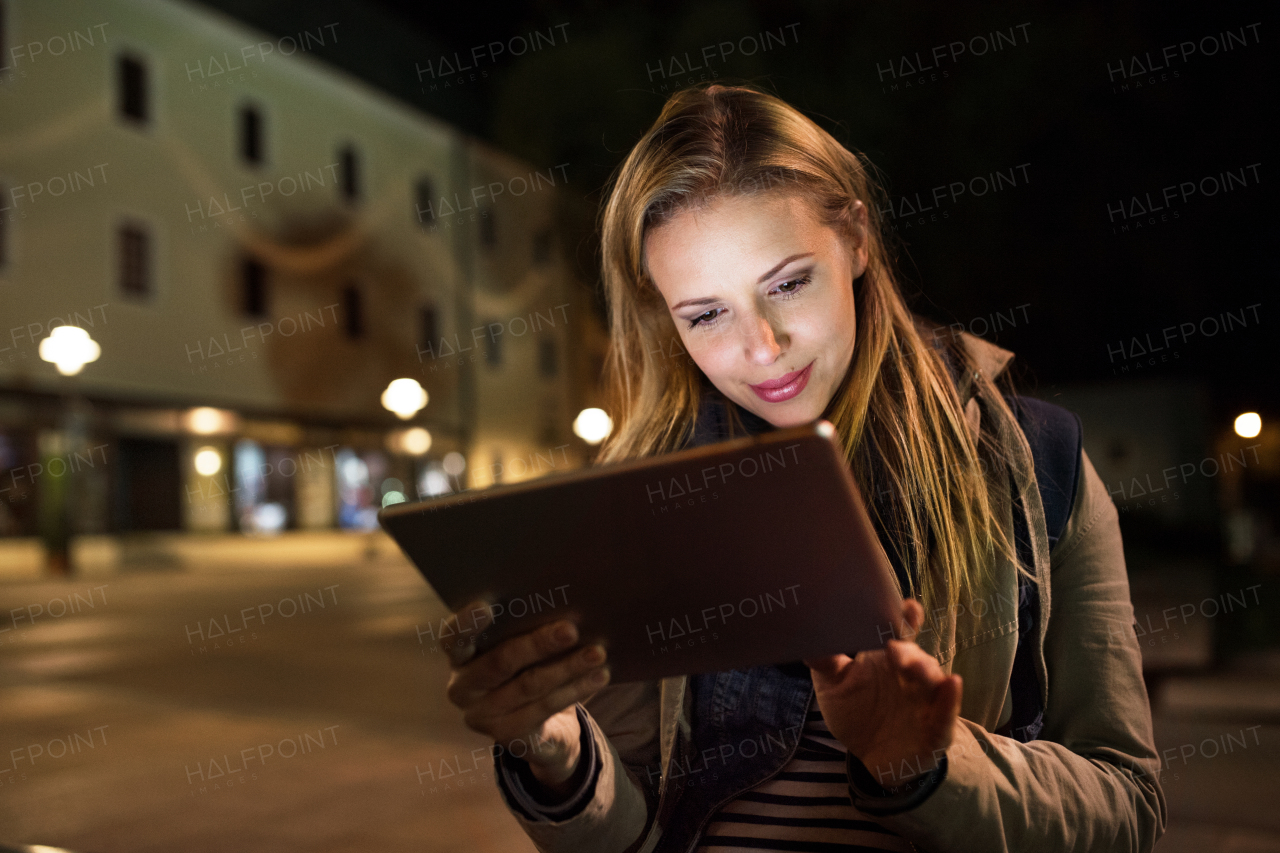 Beautiful woman in the city at night holding tablet, reading something.