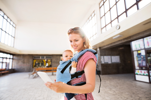 Young mother with smartphone and baby travelling. A beautiful woman and her son inside the station building.