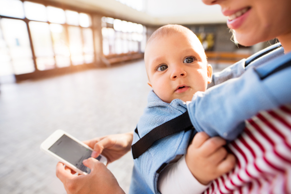 Unrecognizable young mother with smartphone and baby travelling. A beautiful woman and her son inside the station building.