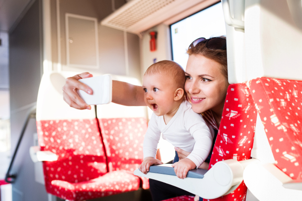 Young mother travelling with baby boy by train. Railway journey of a beautiful woman and her son. A woman taking selfie with a smartphone.