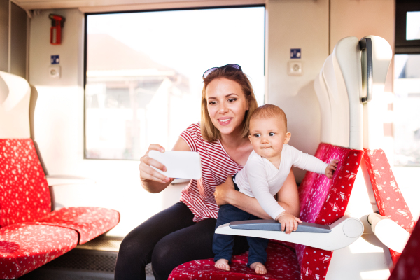 Young mother travelling with baby boy by train. Railway journey of a beautiful woman and her son. A woman taking selfie with a smartphone.