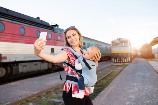 Young mother travelling with baby boy by train. A woman with smartphone and her son at the railway station.