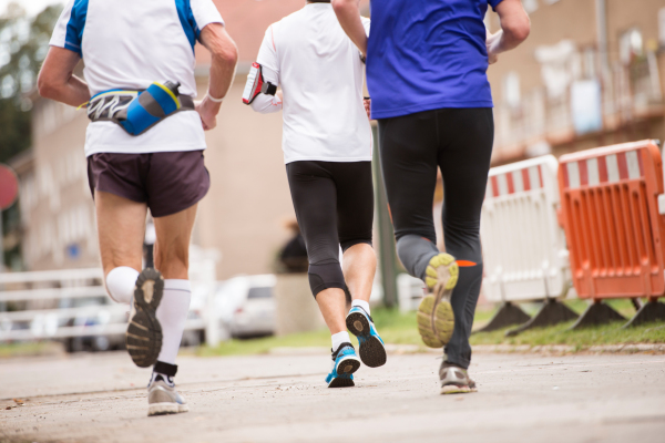 Group of unrecognizable runners sprinting outdoors. Sportive people training in a urban area, healthy lifestyle and sport concepts. Rear view.