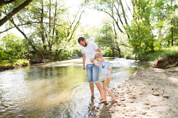 Young father with little boy at the river having fun, entering into the water, sunny spring day.