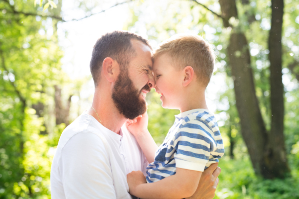 Young father with his little son in green woods holding and hugging him, sunny day.