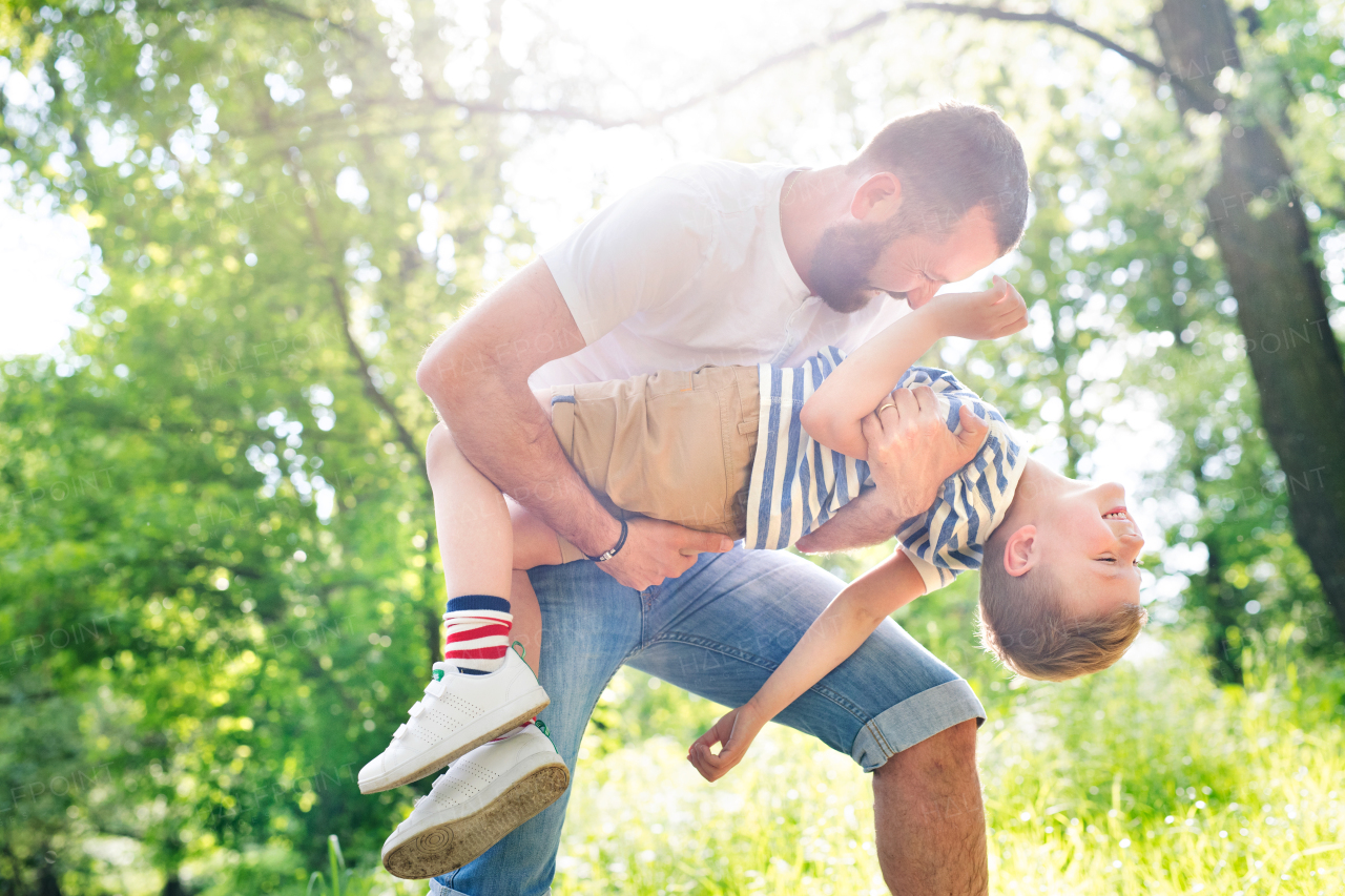 Young father with his little son in green woods holding and hugging him, playing together, sunny day.