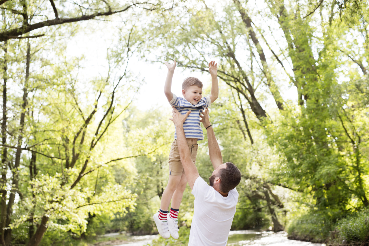 Young father with little boy outside having fun near river, sunny spring day.