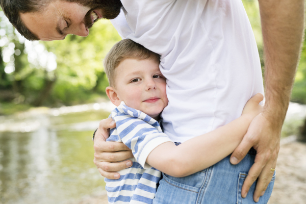 Young father with little boy outside having fun near river, sunny spring day.