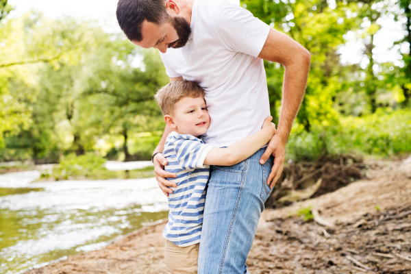 Young father with little boy outside having fun near river, sunny spring day.