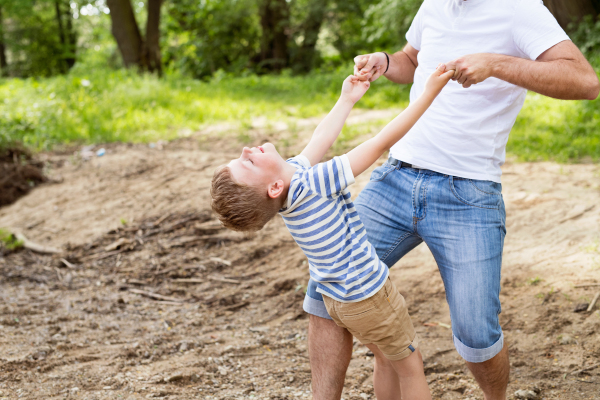 Unrecognizable father with his little son in green woods holding him, playing together, sunny day.