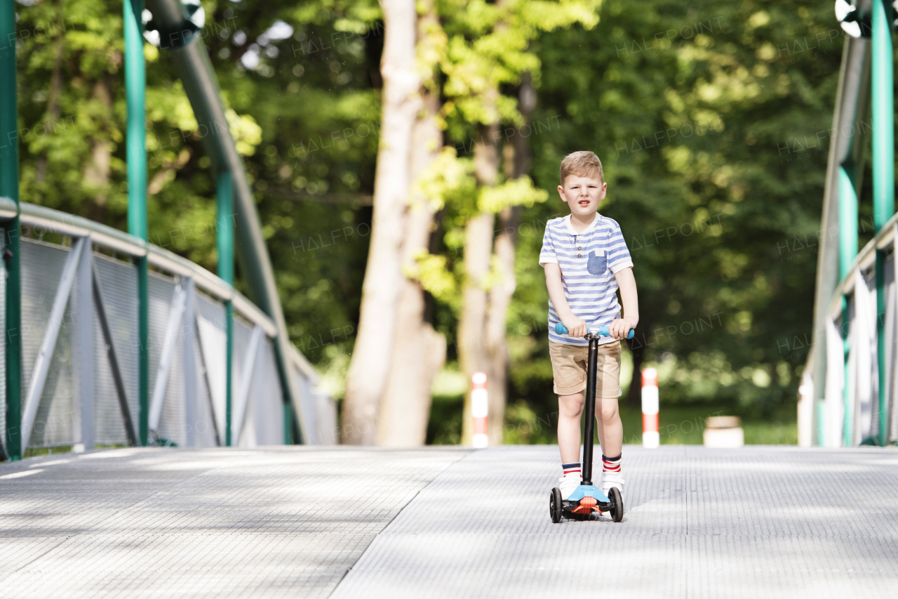 Little boy riding his scooter in the local park. Sunny summer day.