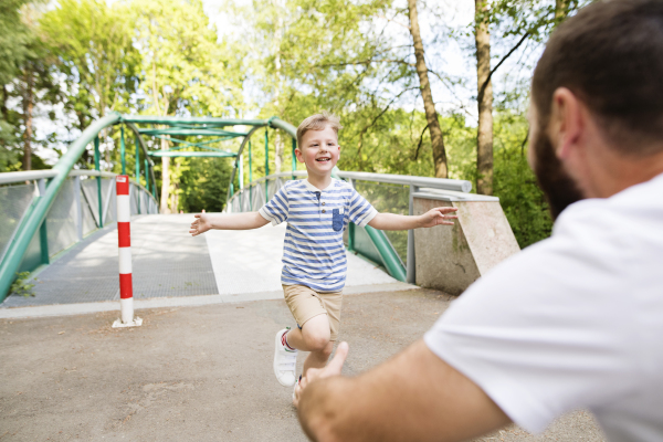 Little boy running into the arms of his father, sunny summer day.