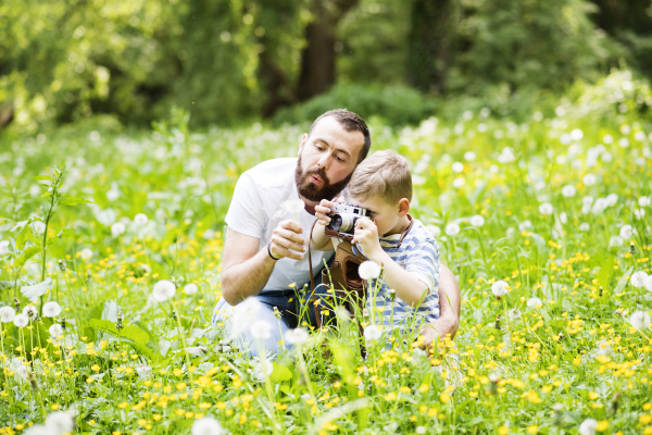 Young hipster father outdoors with his little son with camera, taking pictures of nature. Sunny summer day.