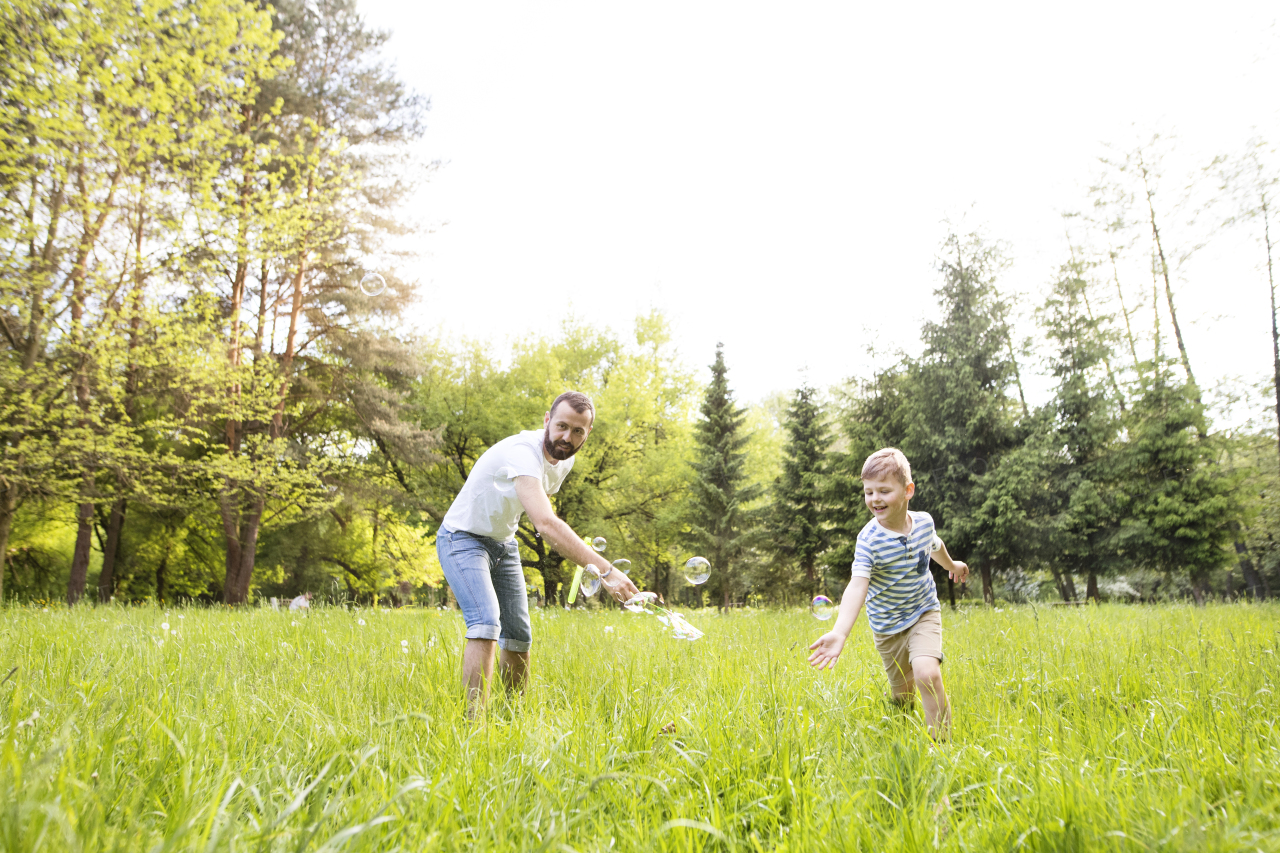 Young hipster father with little boy outside blowing bubbles, having fun, sunny summer day.