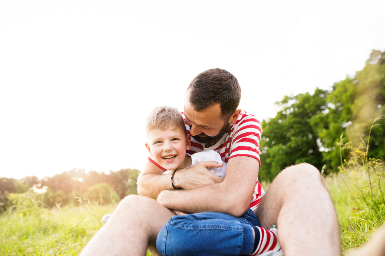 Young hipster father with his little son outside sitting on green meadow. Sunny summer day.