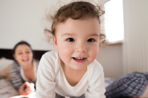 Beautiful young mother with her cute little daughter lying on bed, having fun