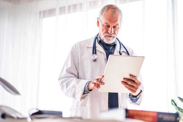 Senior doctor with tablet working in his office.