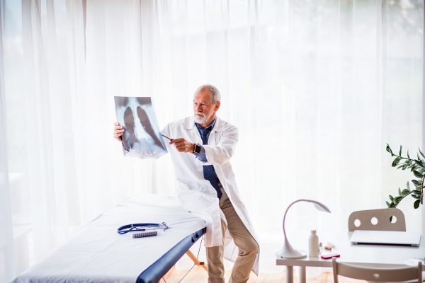 Senior doctor looking at chest x-ray in his office. Male doctor with smartwatch examining an x-ray.