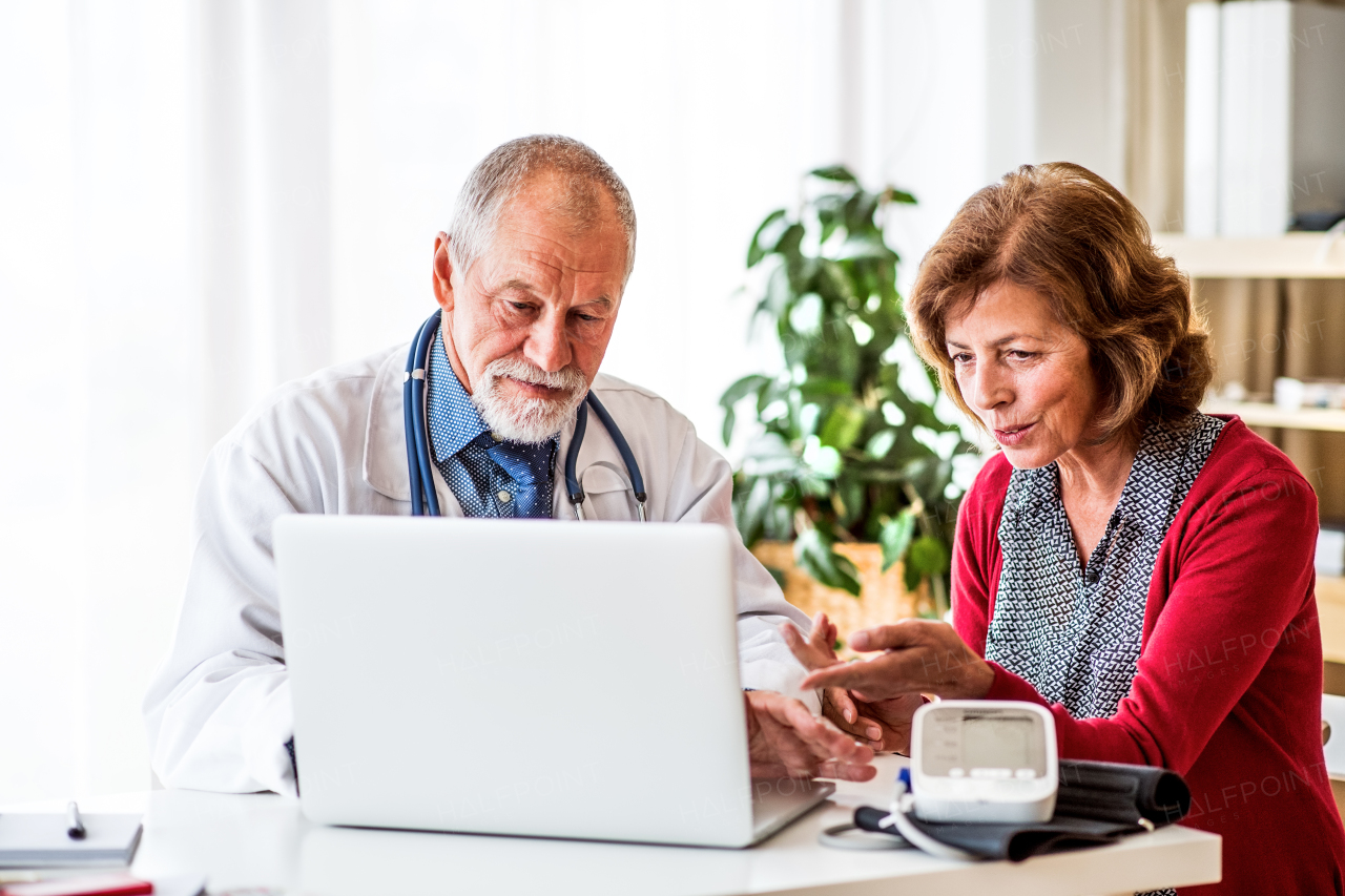 Male doctor with laptop talking to a senior woman in his office.