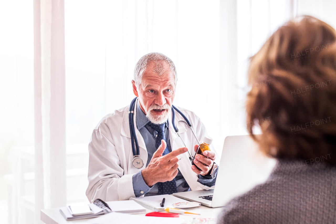 Male doctor with laptop talking to a senior woman in his office.