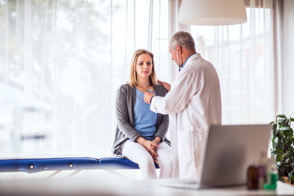 Senior doctor with stethoscope examining a young woman. A doctor and a patient at the doctors office.