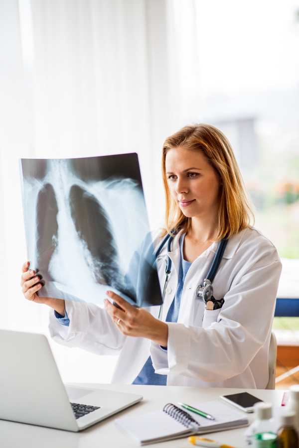 Young female doctor with laptop at the office desk. Doctor examining an x-ray.