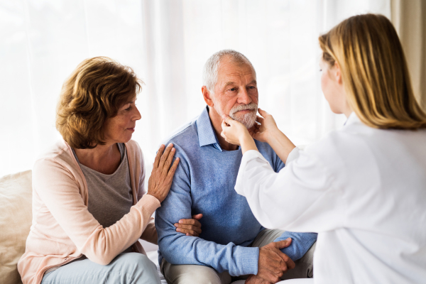 Young female doctor examining a senior man. Senior woman sitting next to man, supporting him.