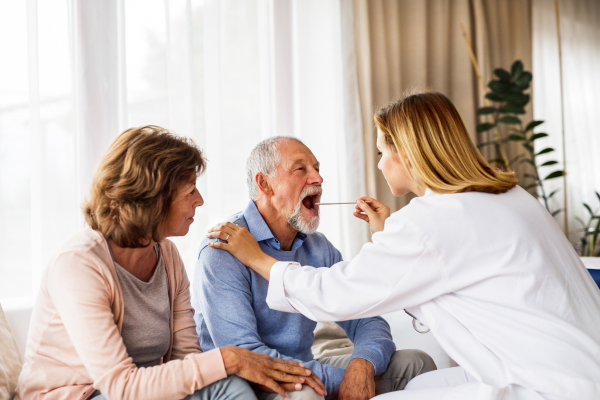 Young female doctor examining a senior man. Senior woman sitting next to man.