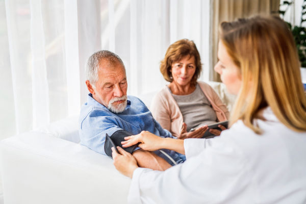 Young female doctor checking blood pressure of senior man. Senior woman holding tablet.