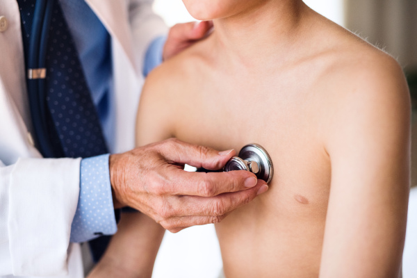 Unrecognizable senior male doctor examining a small boy with stethoscope in his office.