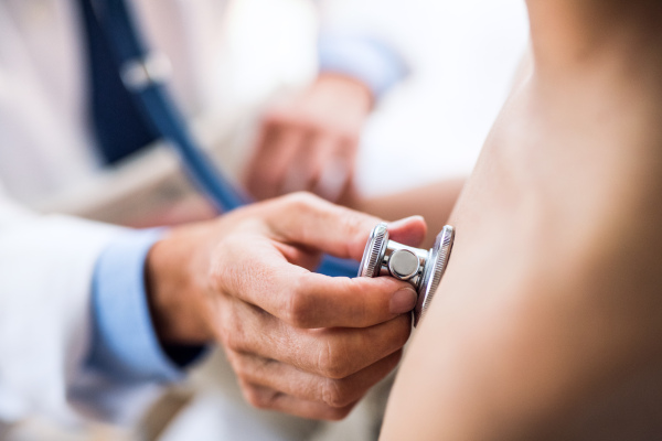 Unrecognizable senior male doctor examining a small boy with stethoscope in his office.