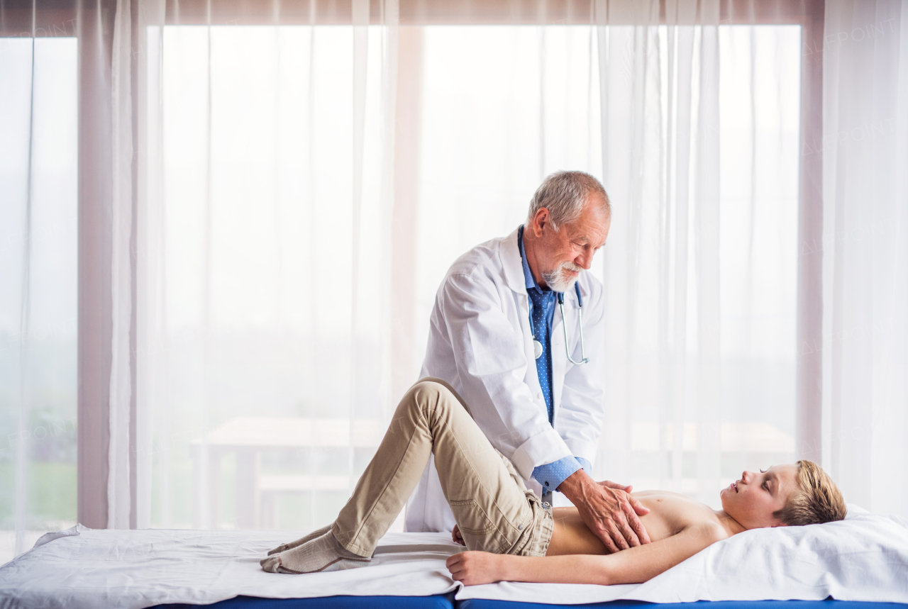 Senior male doctor examining a small boy in his office.