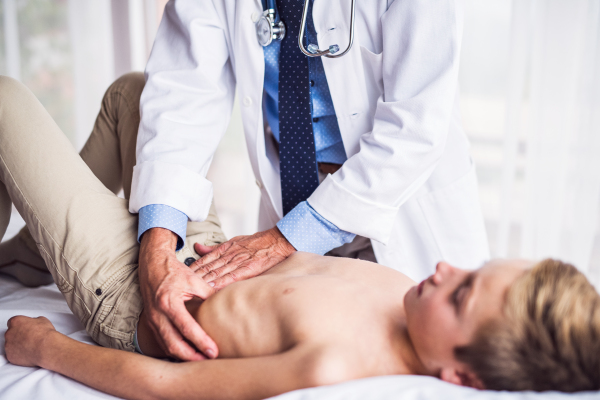 Unrecognizable senior male doctor examining a small boy in his office.