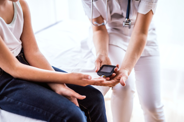 Unrecognizable young female doctor examining a small girl with glucose meter in her office.