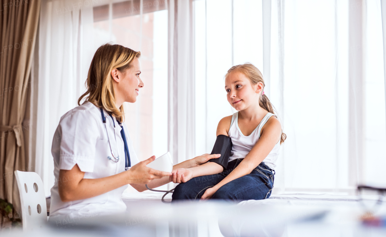 Young female doctor checking blood pressure of a small girl in her office.