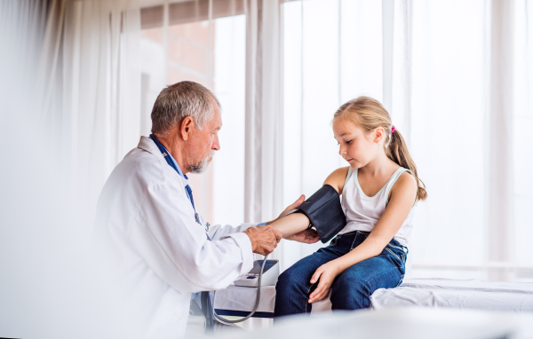 Senior male doctor checking blood pressure of a small girl in his office.