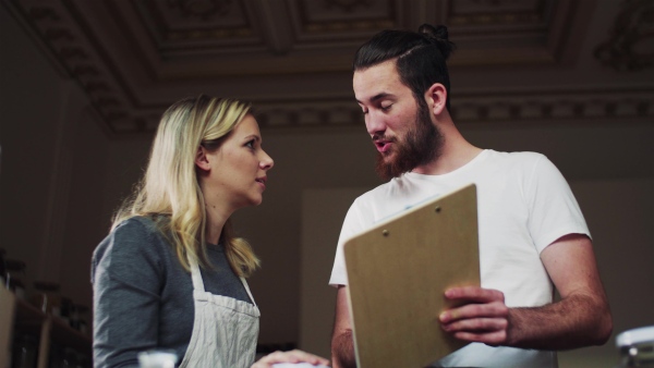 Two young male and female shop assistants with clipboard standing in zero waste shop, talking.