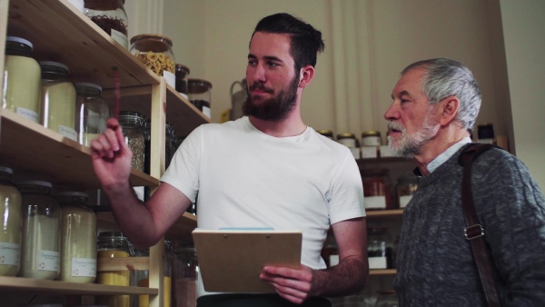 Young shop assistant serving a senior man customer in a zero waste shop.