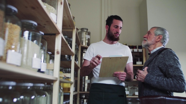 Young shop assistant serving a senior man customer in a zero waste shop.