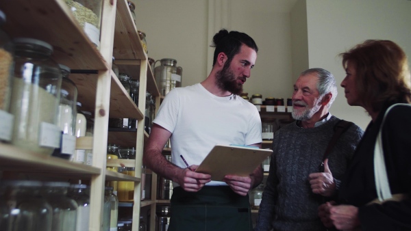 Young shop assistant serving a senior couple customers in a zero waste shop.